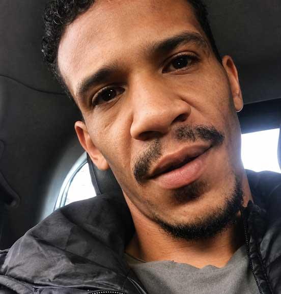 A close-up selfie of Paul Dawson sitting inside a vehicle, wearing a dark jacket and grey shirt. The car window and interior are visible behind him.