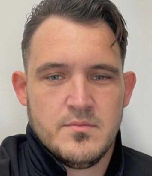 Mugshot 2: Police mugshot of Luke Wall looking slightly to the side, with short hair and an expressionless face, taken in a custody suite.