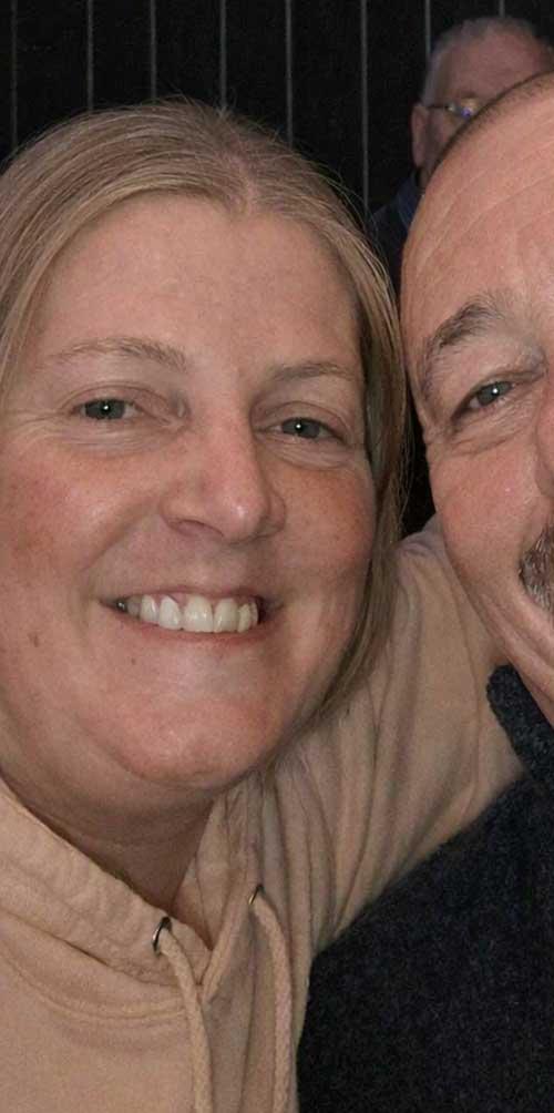 A close-up photo of Michelle Batty indoors. She has light-coloured hair and is wearing a beige hoodie. Another person is partially visible beside her, with a dark background behind them.